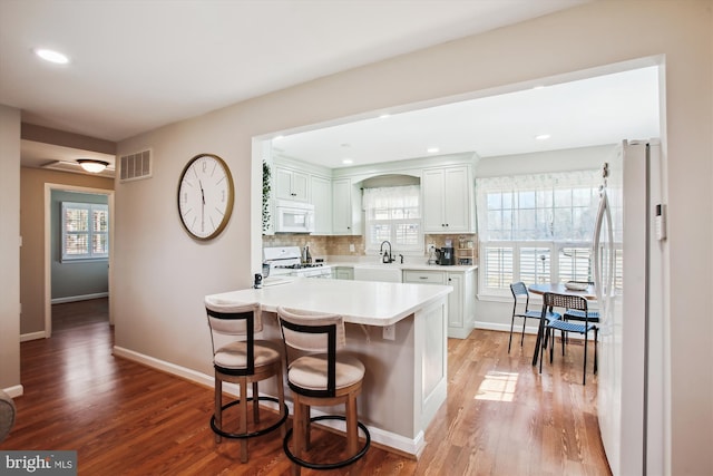 kitchen with visible vents, a sink, tasteful backsplash, white appliances, and a breakfast bar area