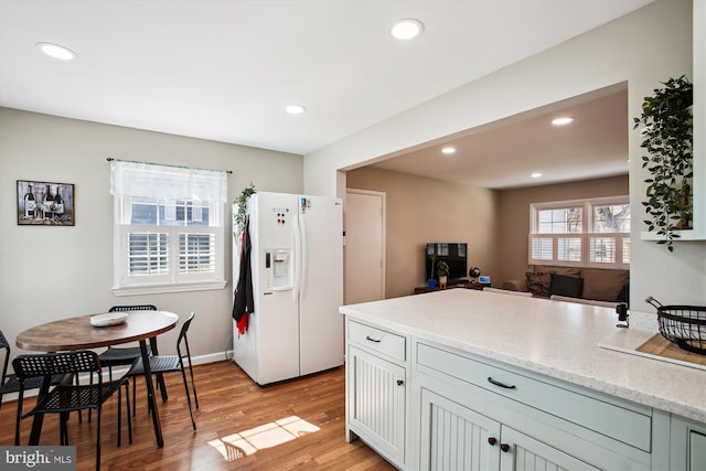 kitchen featuring light wood-style flooring, white refrigerator with ice dispenser, recessed lighting, and light stone countertops