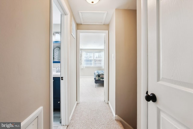 hallway featuring a sink, baseboards, and light carpet