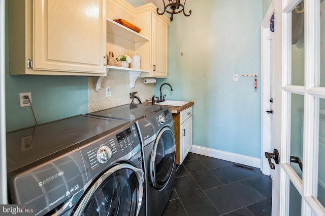 clothes washing area with washing machine and clothes dryer, a sink, baseboards, cabinet space, and dark tile patterned flooring