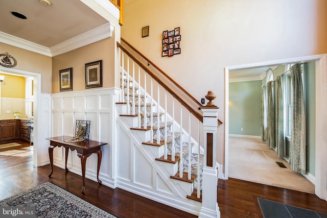 stairs with visible vents, a wainscoted wall, wood finished floors, crown molding, and a decorative wall