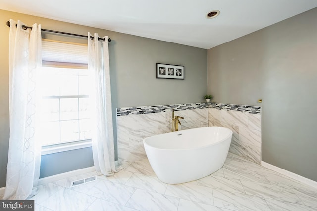 full bathroom featuring a wealth of natural light, visible vents, a soaking tub, and marble finish floor