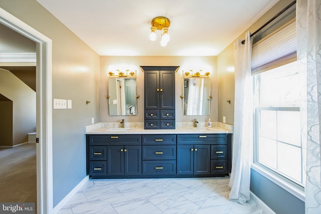 full bath with double vanity, marble finish floor, baseboards, and a sink