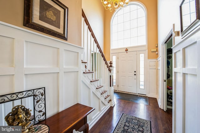 entryway with dark wood-style floors, a high ceiling, a decorative wall, a chandelier, and stairs