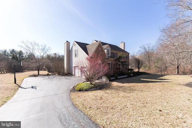 view of home's exterior featuring an attached garage, a chimney, driveway, and a yard