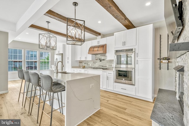 kitchen featuring light wood finished floors, range hood, appliances with stainless steel finishes, a notable chandelier, and a sink