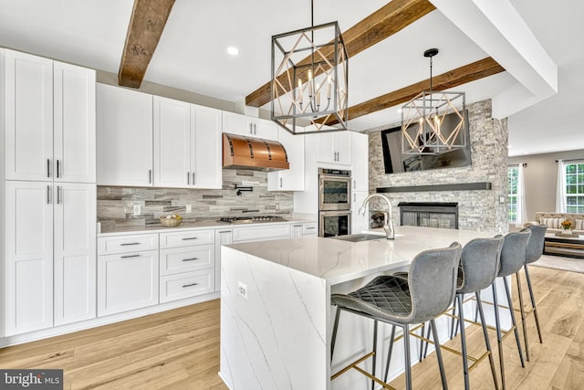 kitchen with light wood finished floors, tasteful backsplash, stainless steel appliances, wall chimney exhaust hood, and a sink