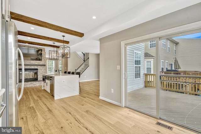 kitchen with beamed ceiling, open floor plan, appliances with stainless steel finishes, a fireplace, and light wood finished floors