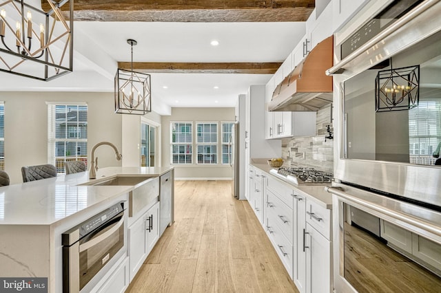 kitchen featuring appliances with stainless steel finishes, white cabinetry, a notable chandelier, light wood-type flooring, and backsplash