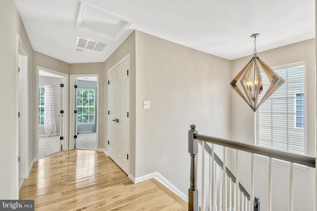 hall with an upstairs landing, attic access, light wood-type flooring, and an inviting chandelier