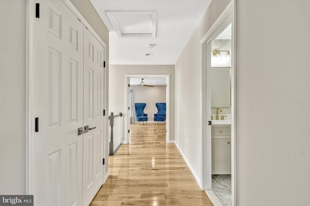 corridor with a sink, light wood-type flooring, baseboards, and attic access