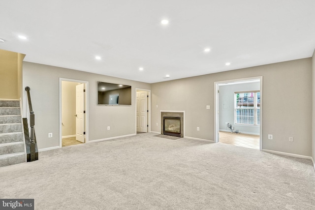 unfurnished living room featuring stairs, recessed lighting, light colored carpet, and a fireplace with flush hearth