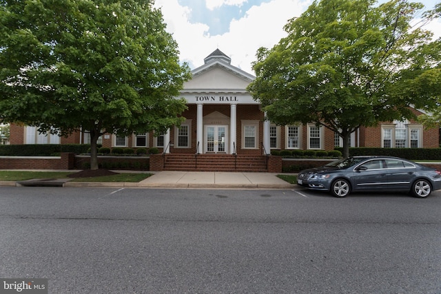 greek revival house featuring brick siding, covered porch, and french doors