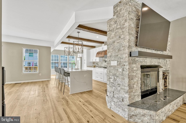 kitchen with under cabinet range hood, a center island with sink, light wood-type flooring, a stone fireplace, and white cabinets