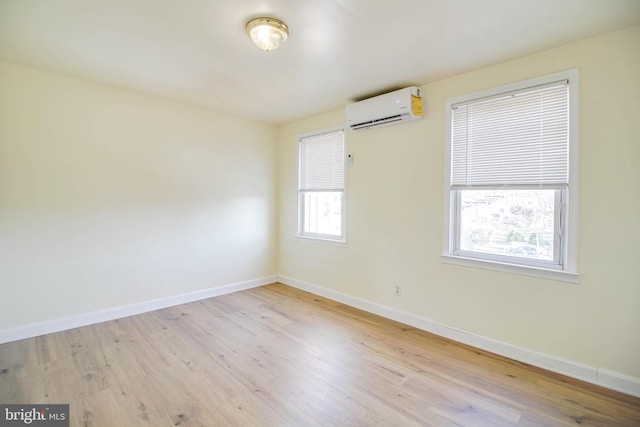 unfurnished room with a wall mounted air conditioner, baseboards, and wood finished floors