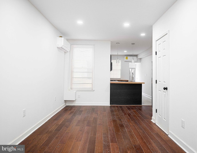 unfurnished living room featuring dark wood finished floors, a wall unit AC, recessed lighting, and baseboards