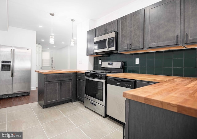 kitchen with light tile patterned floors, a peninsula, butcher block countertops, decorative backsplash, and stainless steel appliances