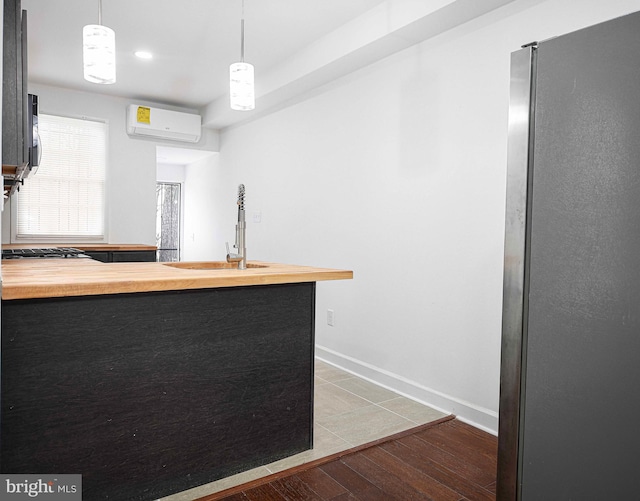 kitchen with butcher block counters, an AC wall unit, a peninsula, freestanding refrigerator, and a sink