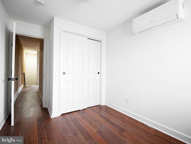 unfurnished bedroom featuring a closet, baseboards, dark wood-style floors, and a wall unit AC