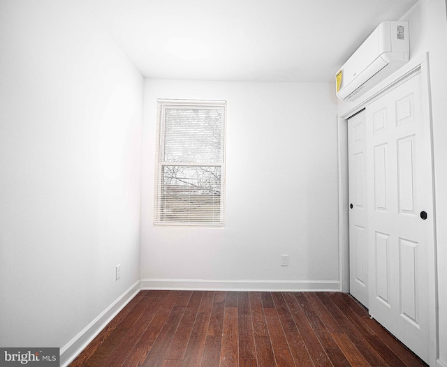 unfurnished bedroom featuring a wall mounted air conditioner, baseboards, and dark wood-style flooring