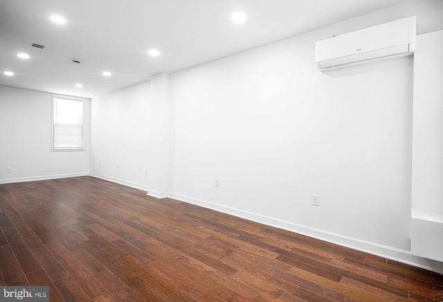 below grade area featuring visible vents, baseboards, dark wood finished floors, an AC wall unit, and recessed lighting