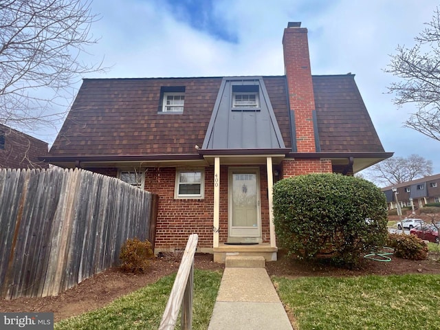 view of front of home featuring brick siding, fence, a chimney, and roof with shingles