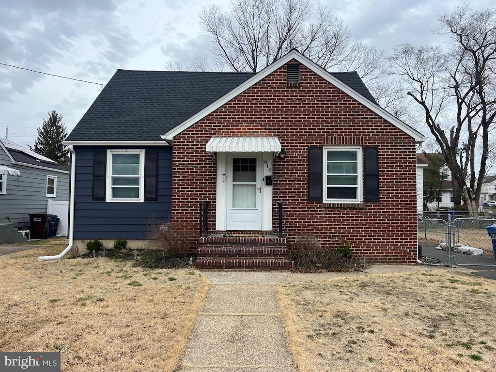 bungalow-style house featuring brick siding, roof with shingles, a front yard, and fence