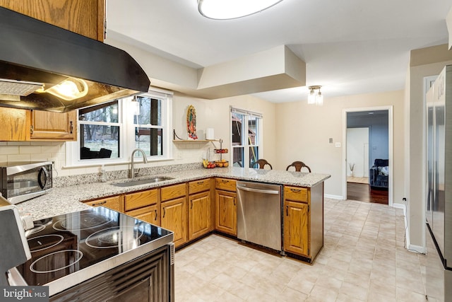 kitchen featuring under cabinet range hood, a sink, tasteful backsplash, stainless steel appliances, and a peninsula