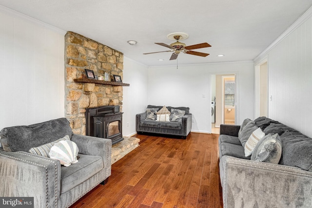 living room featuring crown molding, a wood stove, wood finished floors, washer / clothes dryer, and a ceiling fan