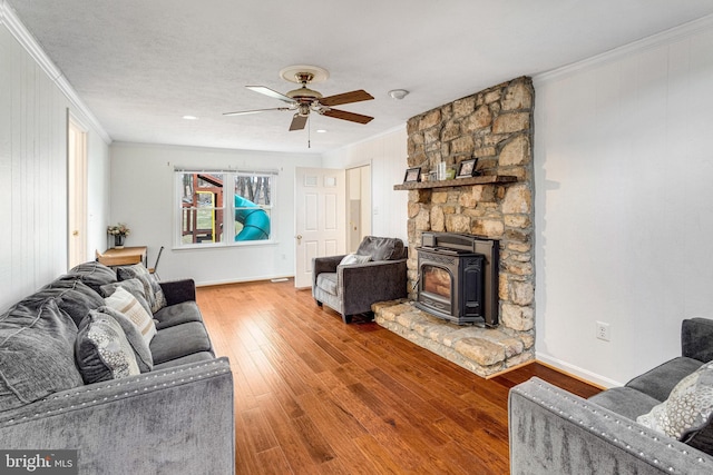 living area featuring ornamental molding, hardwood / wood-style flooring, baseboards, ceiling fan, and a wood stove