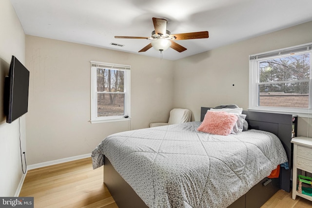 bedroom with a ceiling fan, light wood-style floors, visible vents, and baseboards