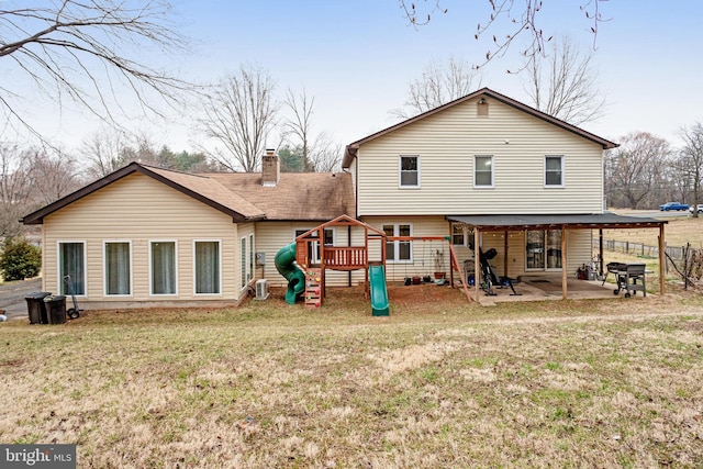 rear view of house with a patio, fence, a chimney, a playground, and a lawn