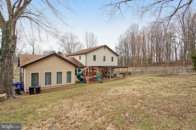 rear view of house with a playground, a lawn, a chimney, and fence