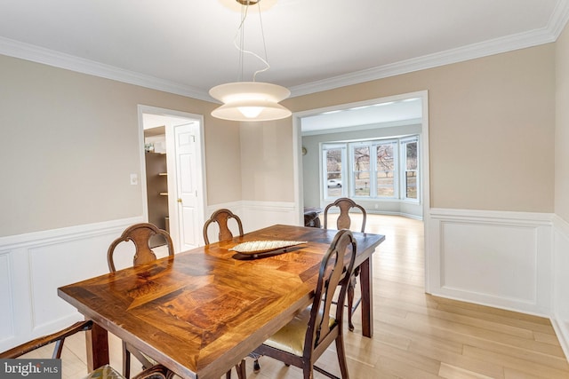 dining room with crown molding, light wood-style floors, and wainscoting