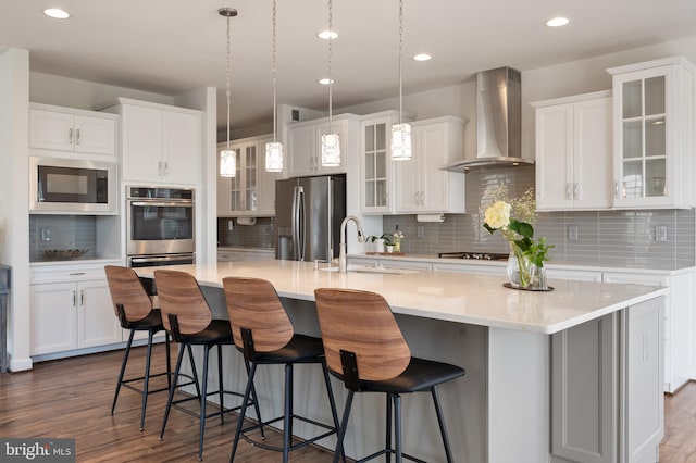 kitchen with wall chimney exhaust hood, tasteful backsplash, appliances with stainless steel finishes, and a center island with sink