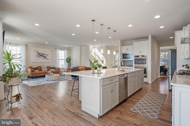 kitchen with a sink, open floor plan, white cabinets, appliances with stainless steel finishes, and an island with sink