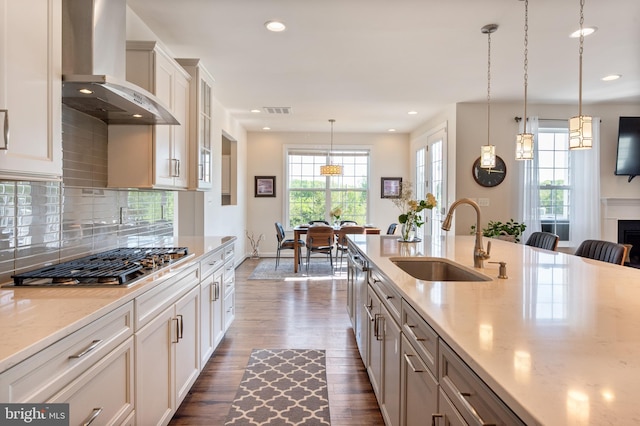 kitchen with stainless steel gas stovetop, wall chimney range hood, dark wood-style flooring, a sink, and visible vents