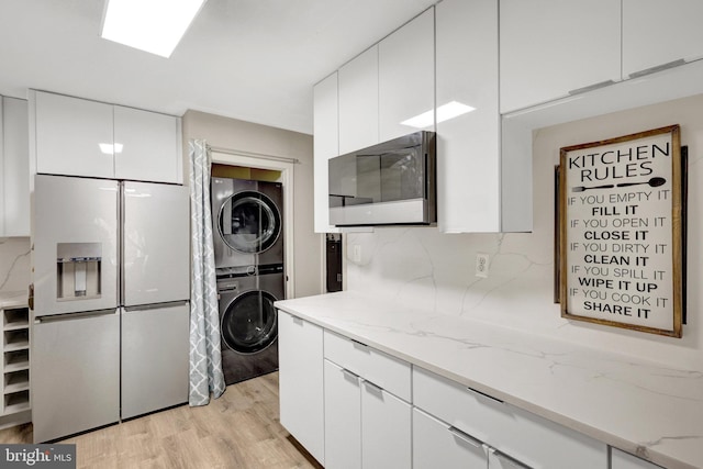 kitchen featuring white cabinets, refrigerator with ice dispenser, light stone countertops, and stacked washer / drying machine