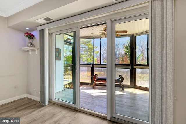 doorway with visible vents, baseboards, light wood-style floors, and ornamental molding