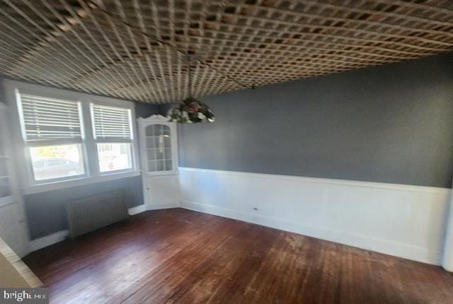 unfurnished dining area featuring radiator heating unit, wood finished floors, and a wainscoted wall