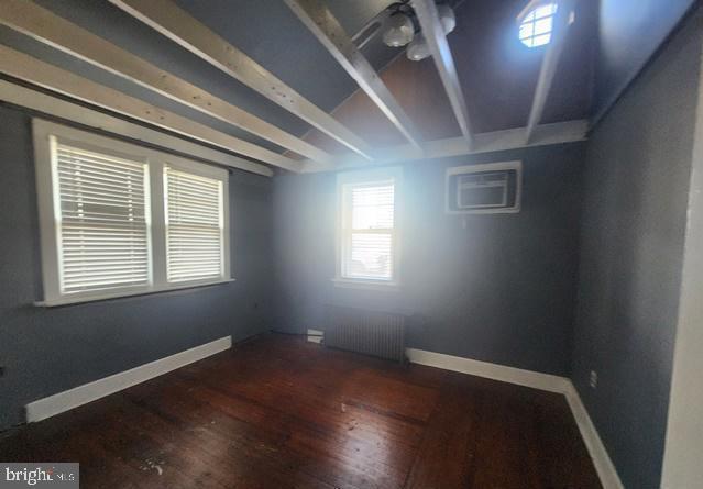 spare room with an AC wall unit, radiator, wood finished floors, and baseboards