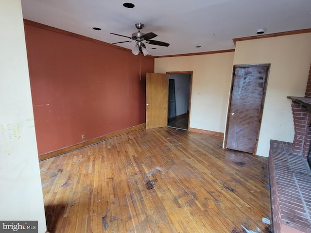 unfurnished living room with a ceiling fan, hardwood / wood-style flooring, crown molding, baseboards, and a brick fireplace