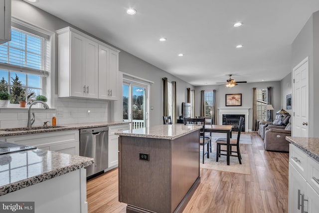 kitchen featuring light wood-type flooring, stainless steel dishwasher, a glass covered fireplace, a ceiling fan, and a sink