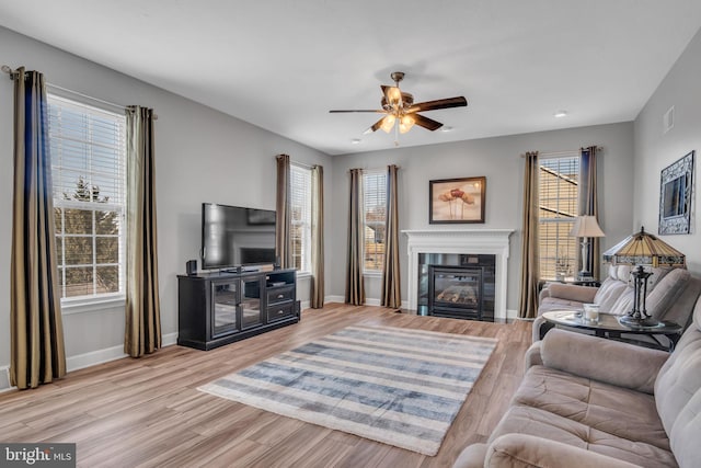 living room with a glass covered fireplace, baseboards, light wood finished floors, and ceiling fan