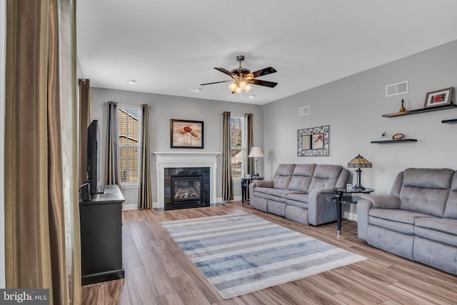 living area with a glass covered fireplace, plenty of natural light, visible vents, and wood finished floors