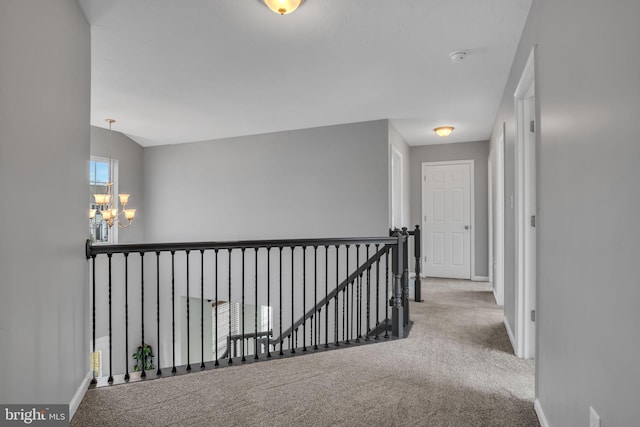 corridor featuring an inviting chandelier, an upstairs landing, carpet, and baseboards