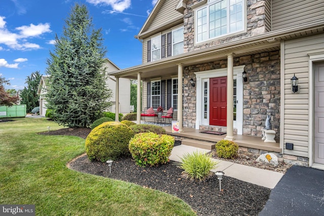 view of exterior entry with a yard, stone siding, and covered porch