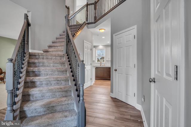 staircase with recessed lighting, baseboards, a towering ceiling, and wood finished floors