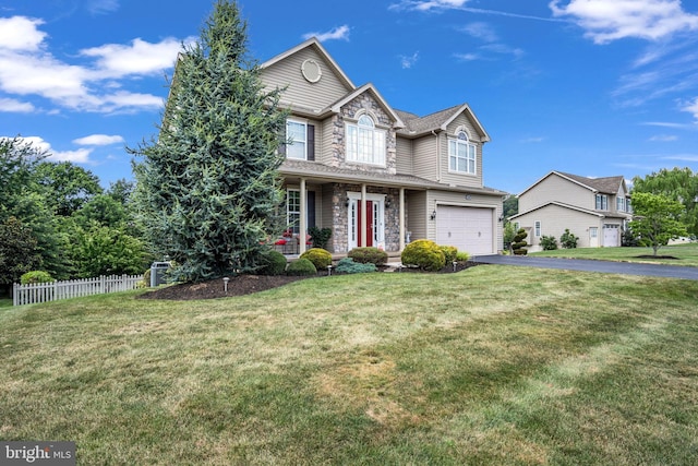 view of front of house with a front yard, fence, a garage, stone siding, and aphalt driveway