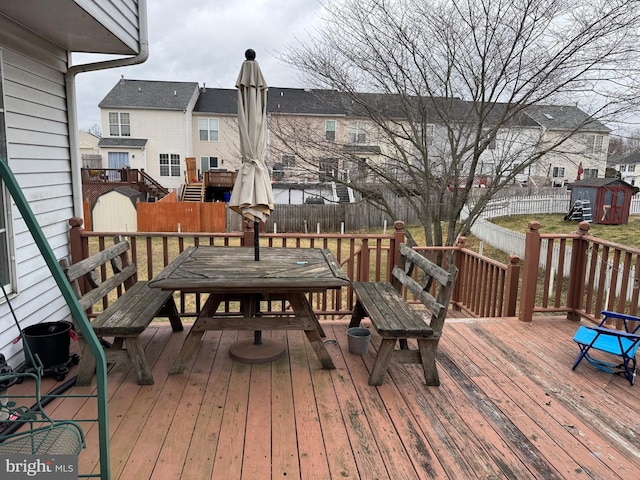 wooden deck featuring an outdoor structure, a fenced backyard, a residential view, and a shed